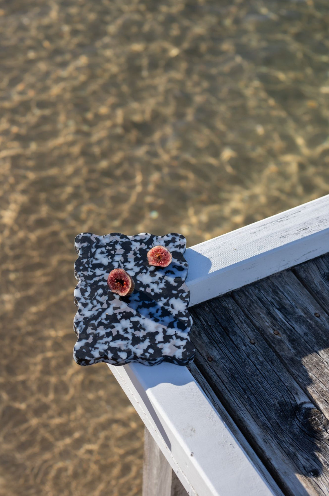 Black and white wavy Pinchy board with figs on wooden jetty over water