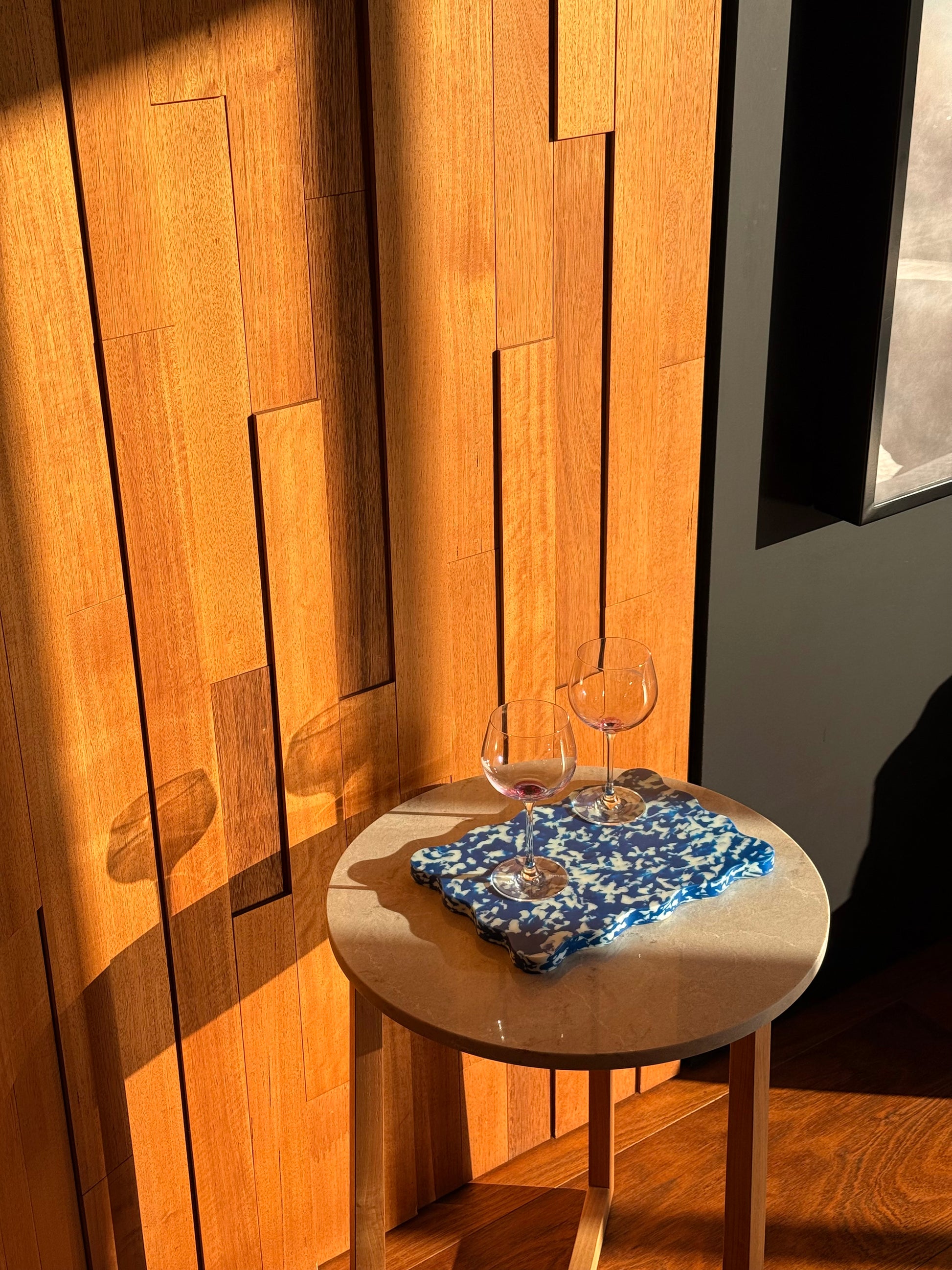 Mid-century wood-panel home interior with blue and white Pinchy chopping board on round table beside wine glasses