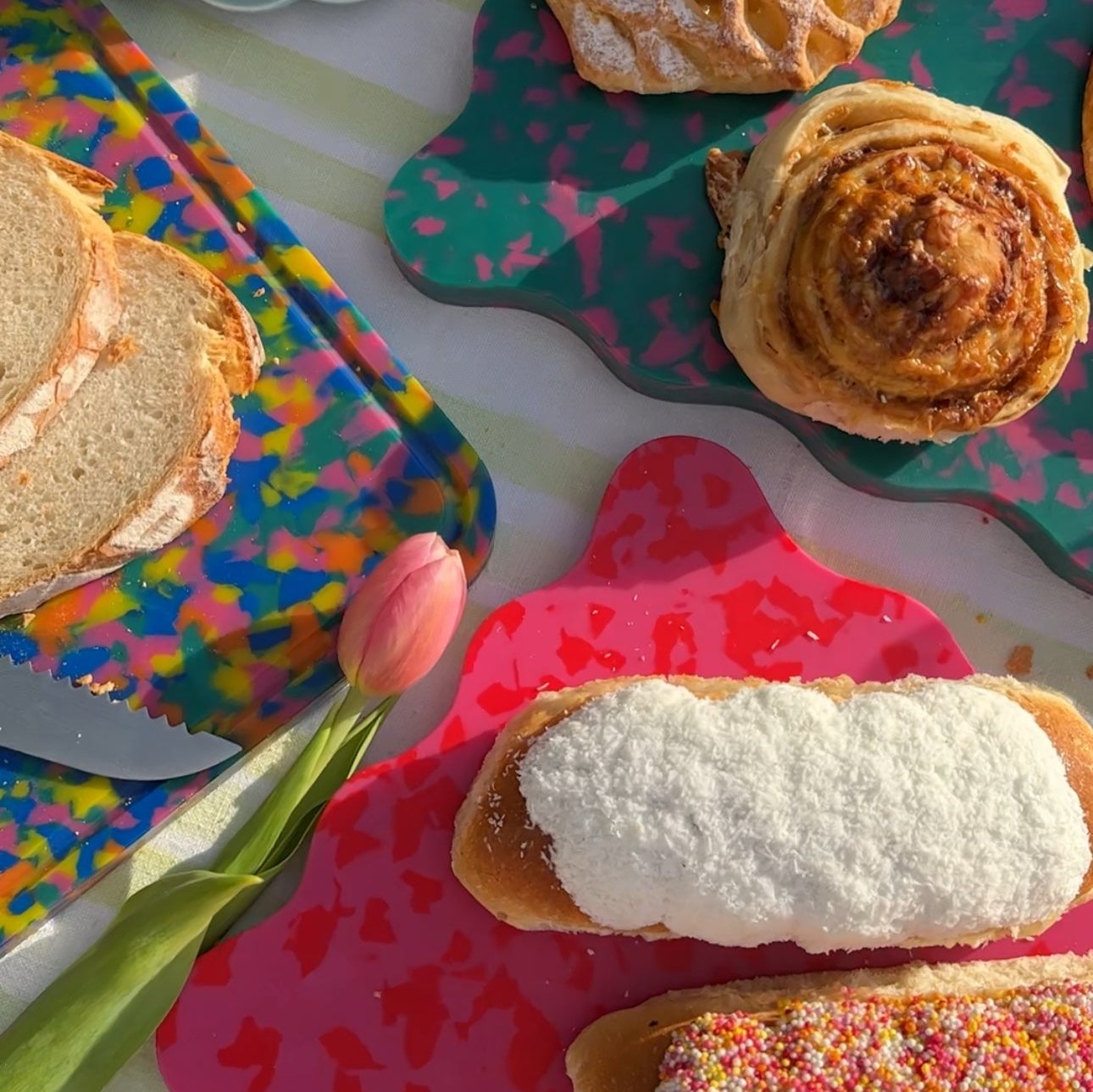 Colourful Pinchy chopping boards with bread and pastries on striped tablecloth in sunlight