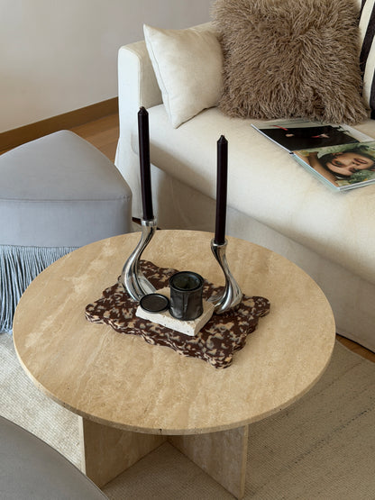 A round light beige stone coffee table in a modern living room setting, styled with a brown and cream wavy Pinchy tray/cutting board.