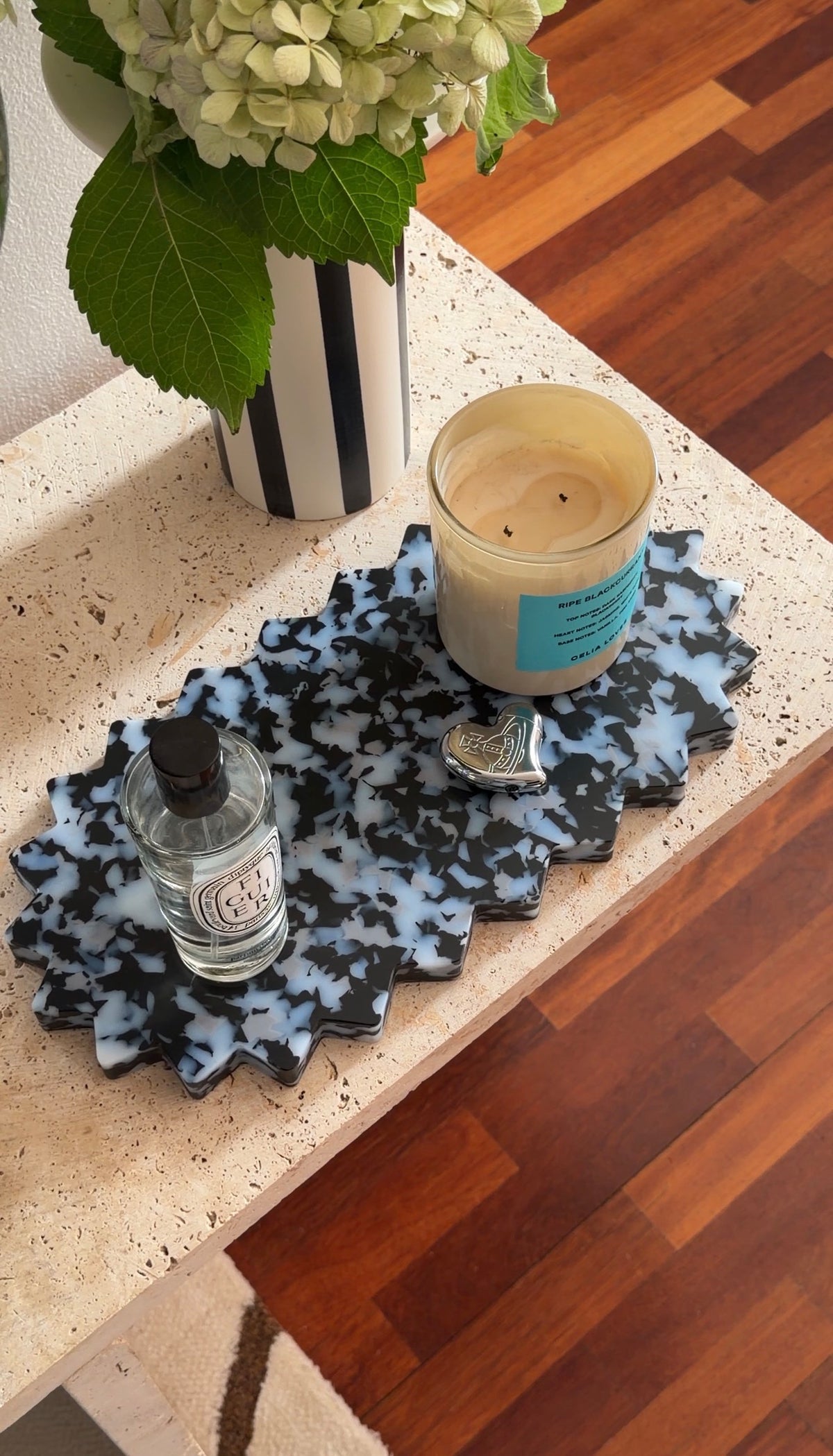 Decorative black and white patterned tray with candle, and vase on a surface.