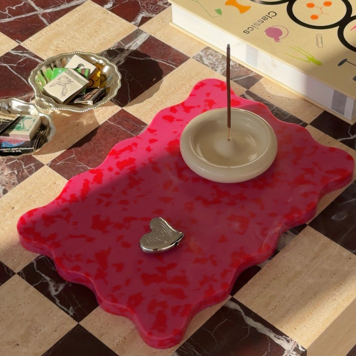 A vibrant pink and red scalloped wavy cutting board by Pinchy used as a decorative centerpiece on a coffee table.